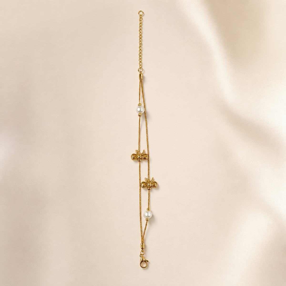 Double-chain bow and pearl-style bracelet laid on pale satin