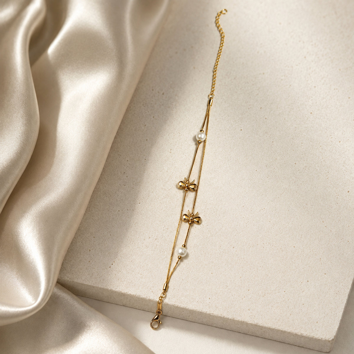 Gold-tone bow bracelet placed on a pale stone slab beside satin
