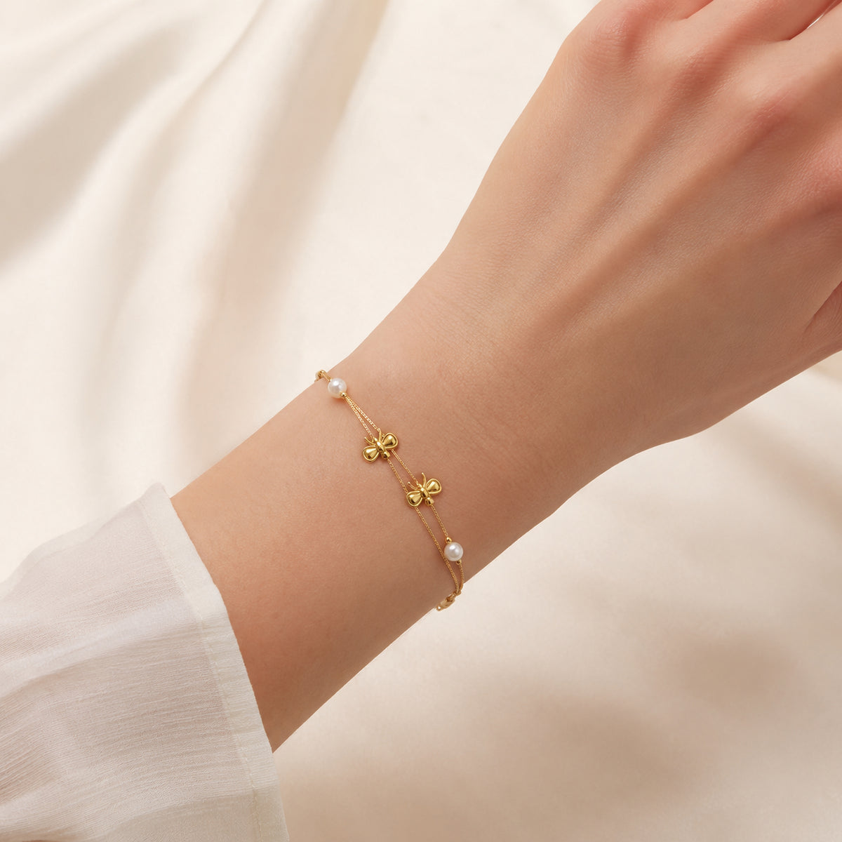 Bow and pearl-style double-chain bracelet shown on a wrist for scale