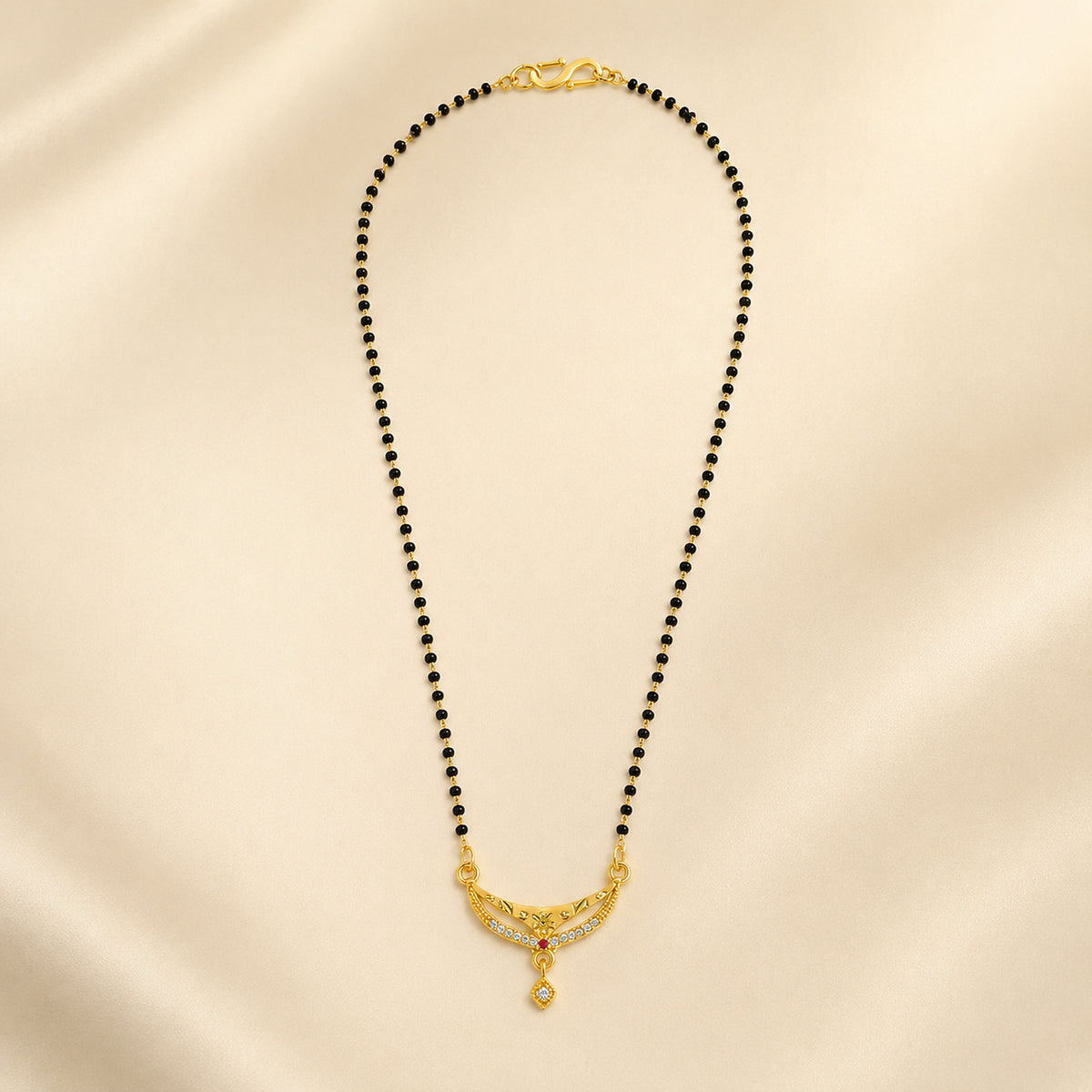 Black bead mangalsutra with curved pendant arranged on cream fabric