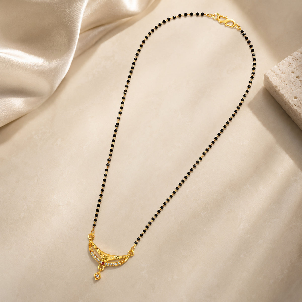 Curved-pendant black bead mangalsutra beside cream display blocks