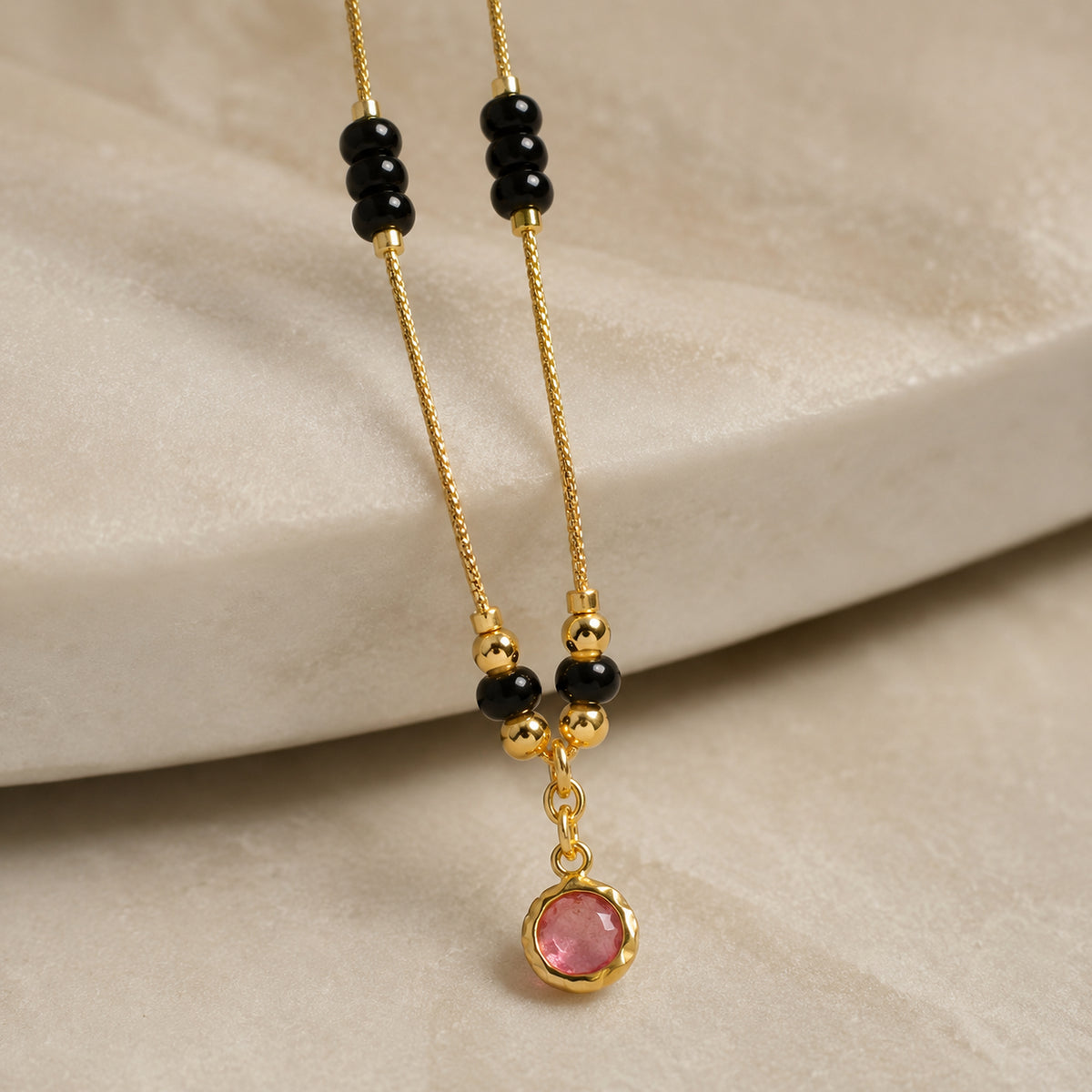 Close-up of the round pink pendant beneath black and gold-tone bead details