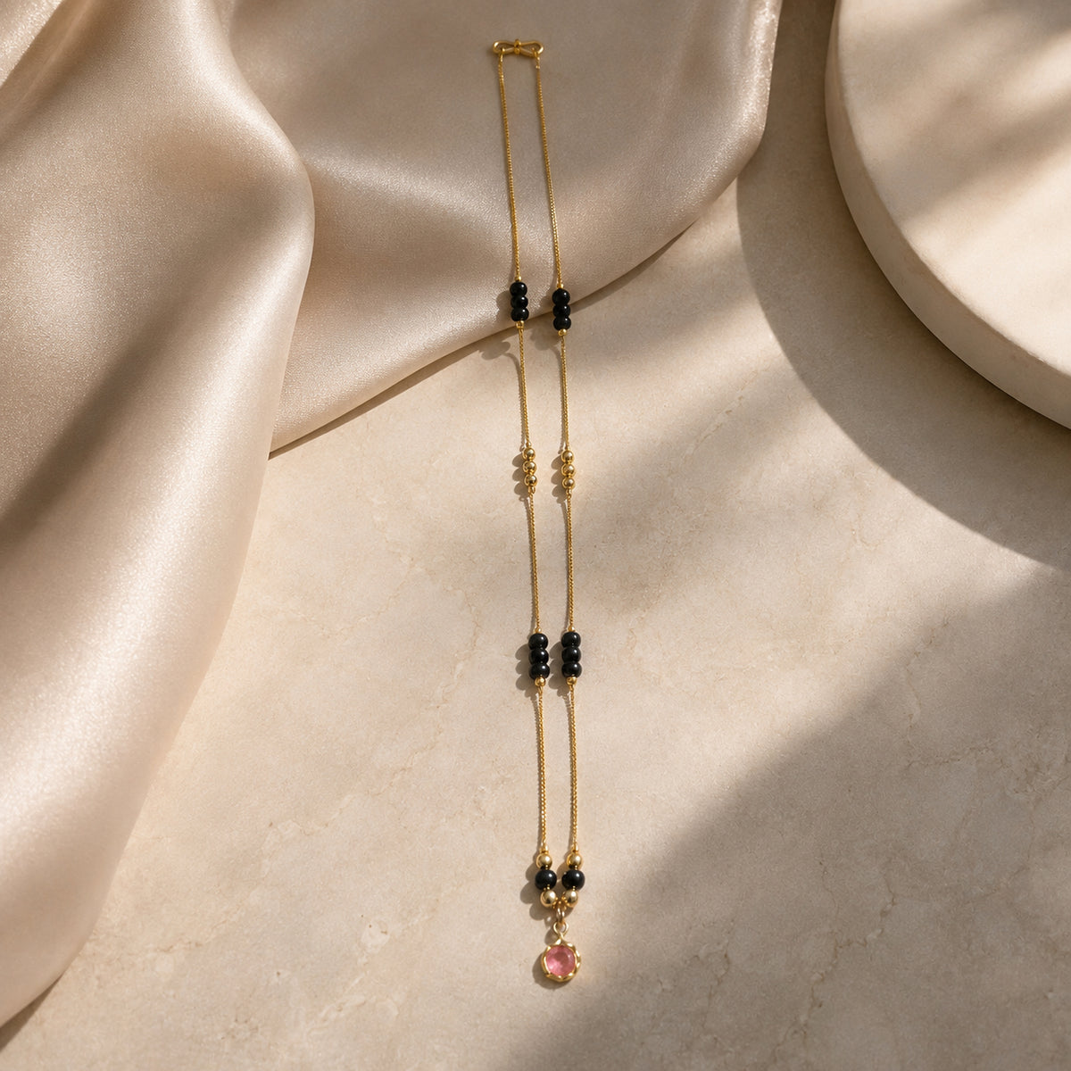 Pink-pendant mangalsutra draped over a cream display block