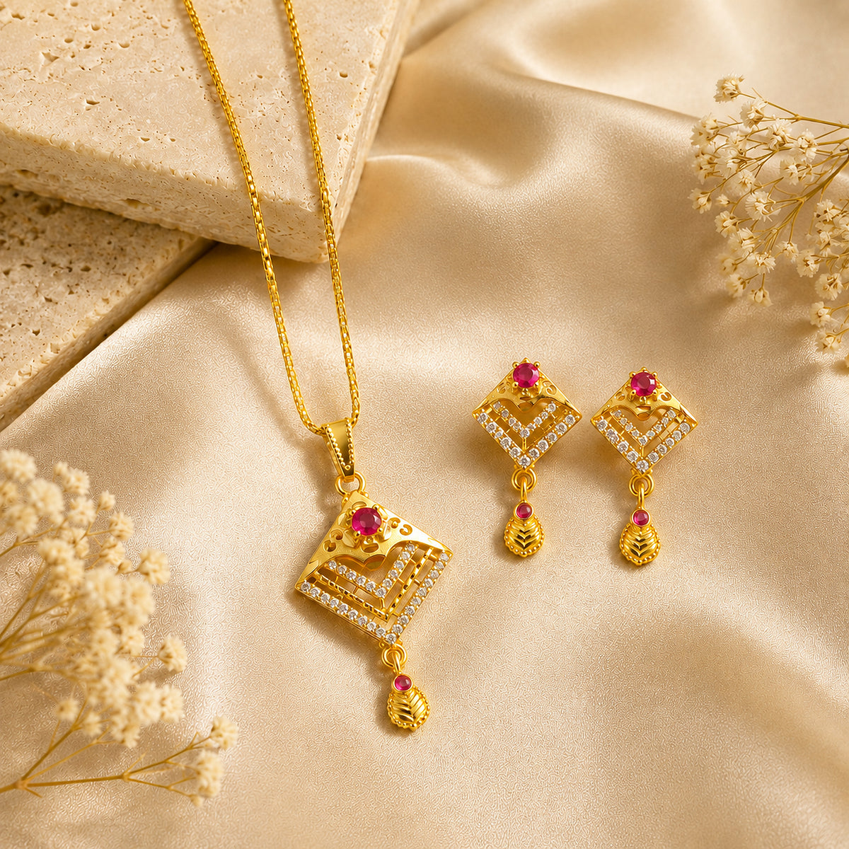 Diamond-shaped chevron pendant and red-stone earrings beside satin and pale stone