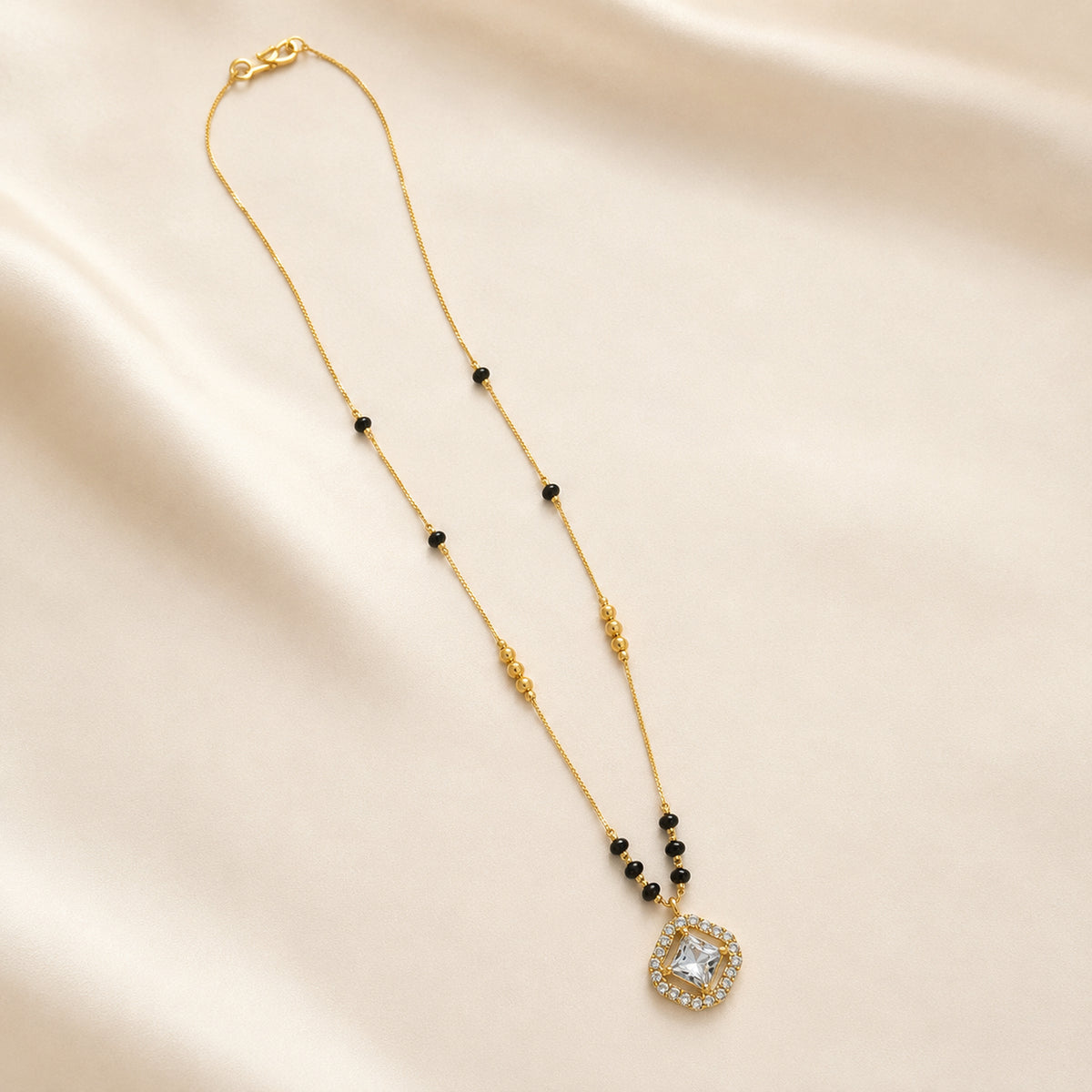 Gold-tone black bead mangalsutra with square pendant on folded fabric