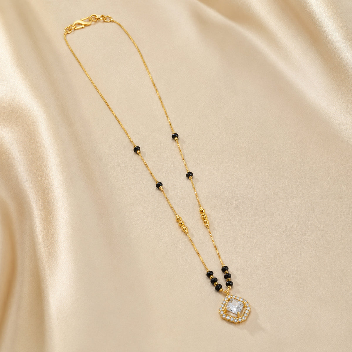 Square clear-stone pendant mangalsutra arranged on cream fabric