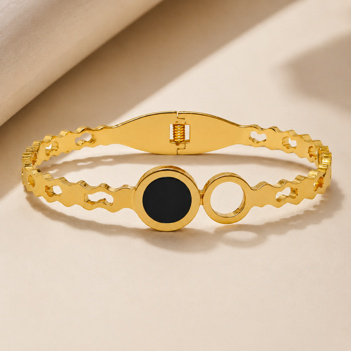 Black disc and open-circle bangle on pale fabric beside satin
