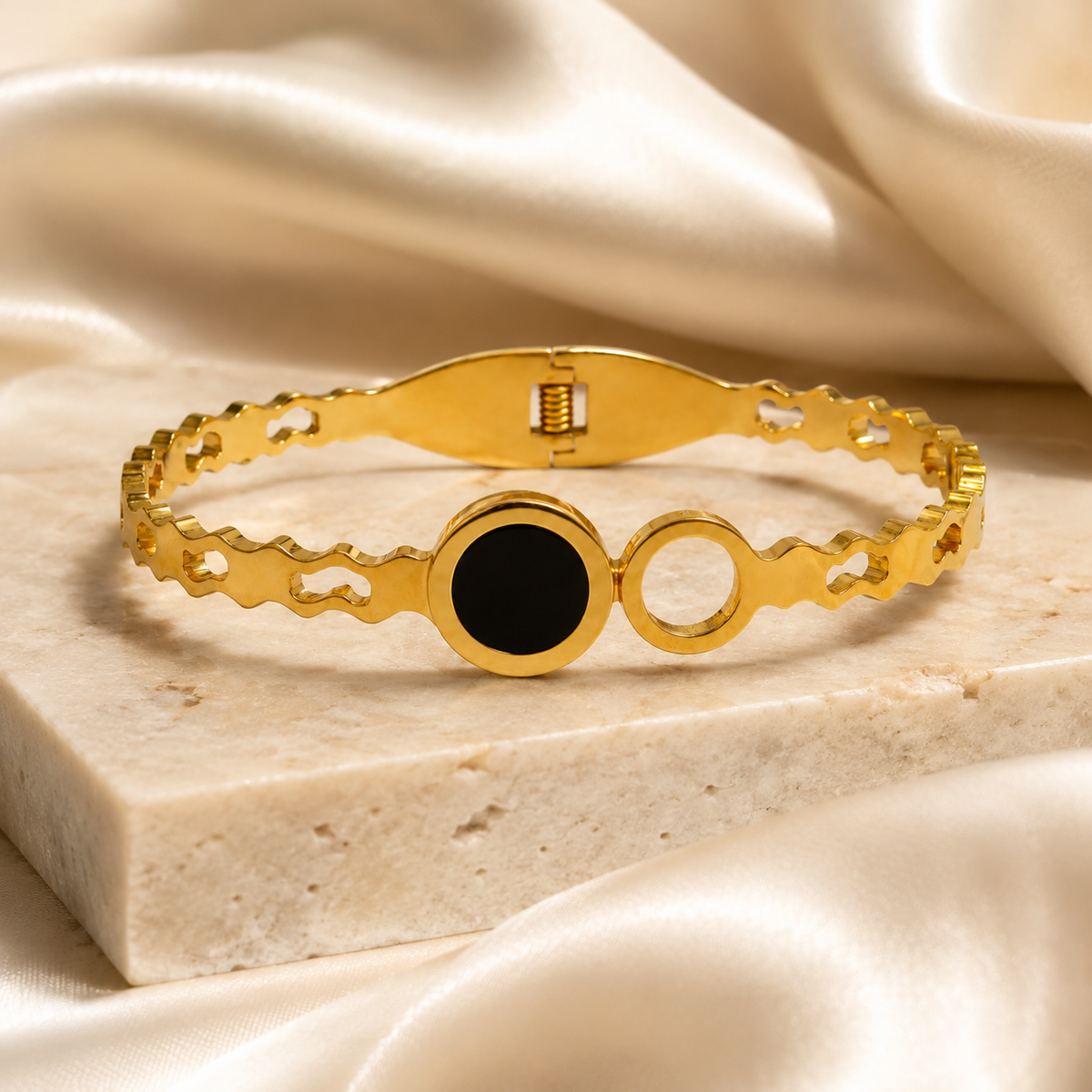 Black and gold-tone geometric bangle displayed on a pale stone base