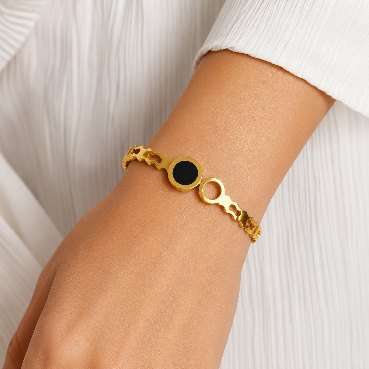 Black disc and open-circle bangle shown on a wrist beside a white sleeve