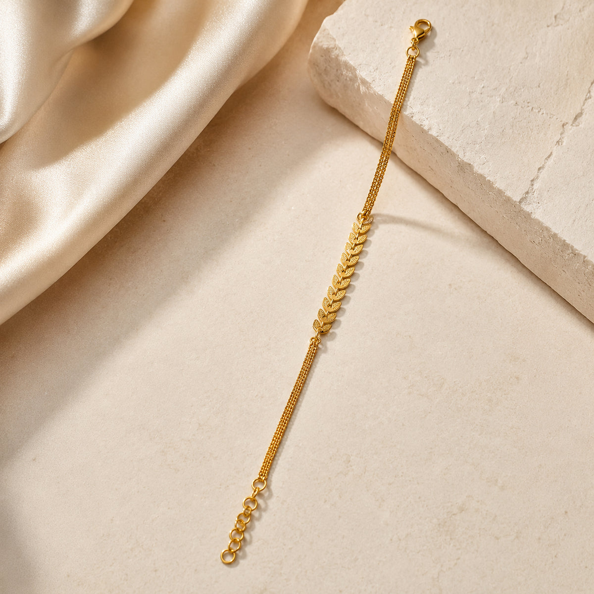 Leaf chain bracelet styled beside a pale stone block and satin