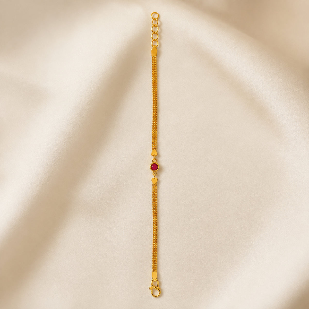 Red stone and heart accent bracelet laid straight on ivory satin