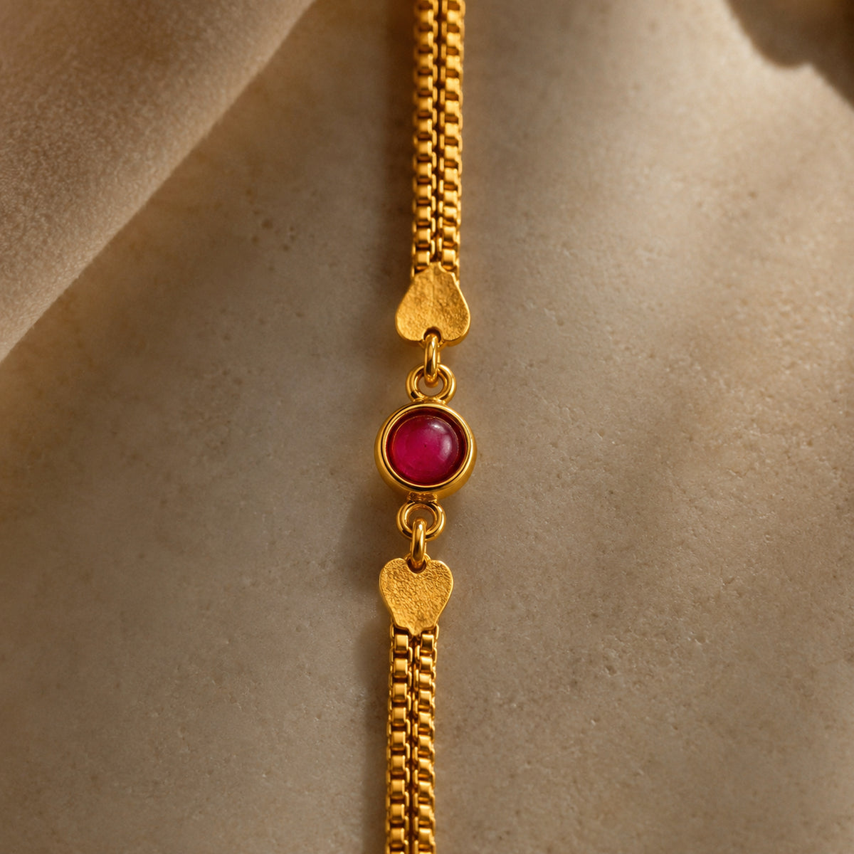 Close-up of the round red-pink stone, heart accents and fine chains