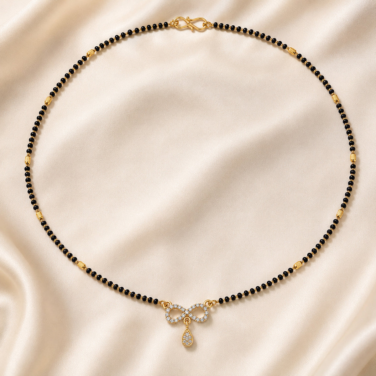 Infinity-pendant black bead mangalsutra arranged on cream fabric