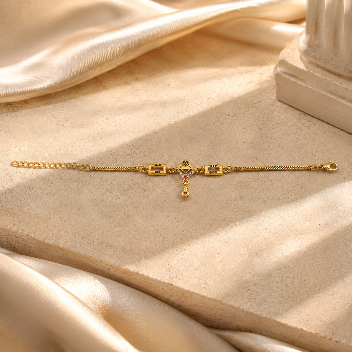 Gold-tone charm bracelet laid beside ivory fabric and a pale column