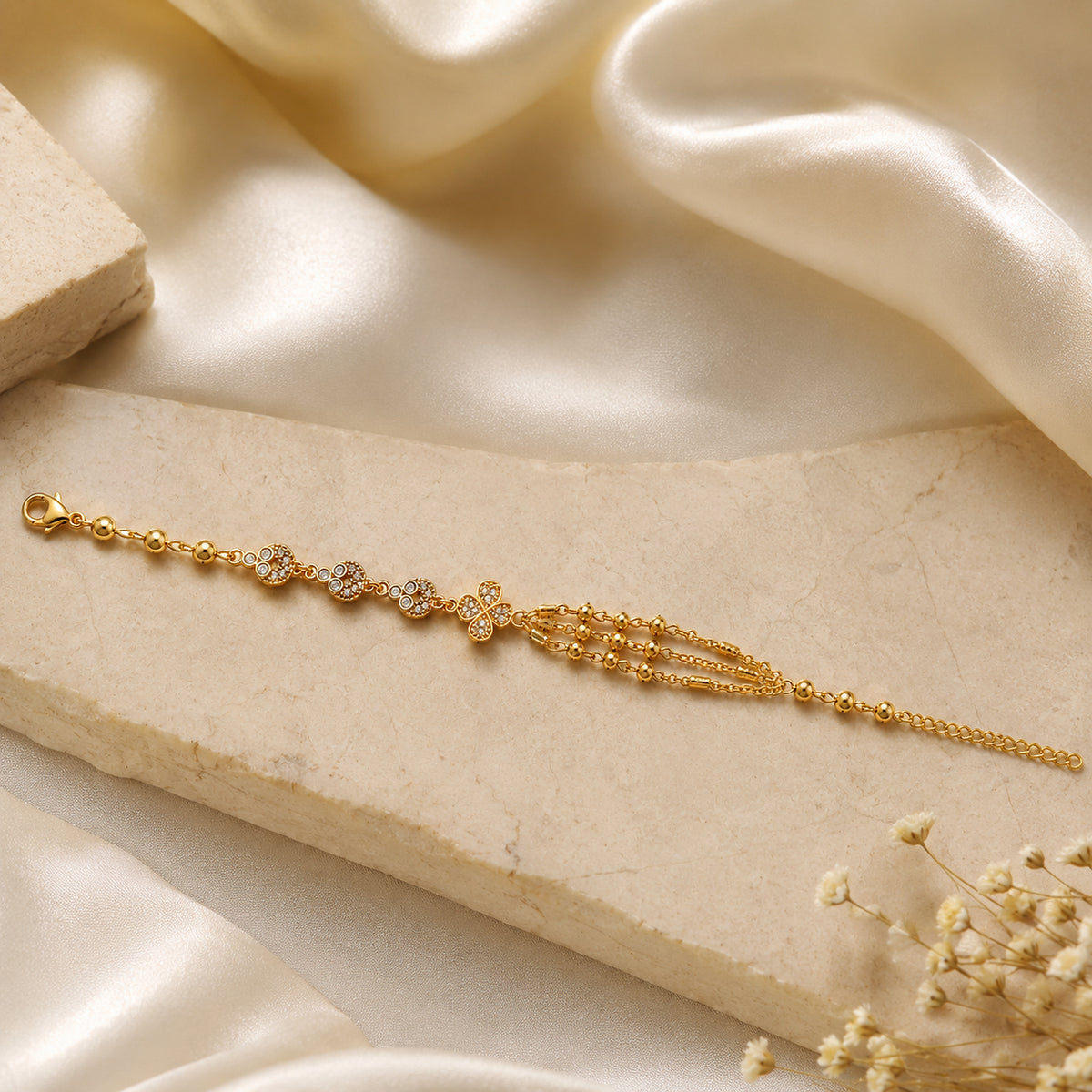 Gold-tone floral chain bracelet on a pale slab with satin