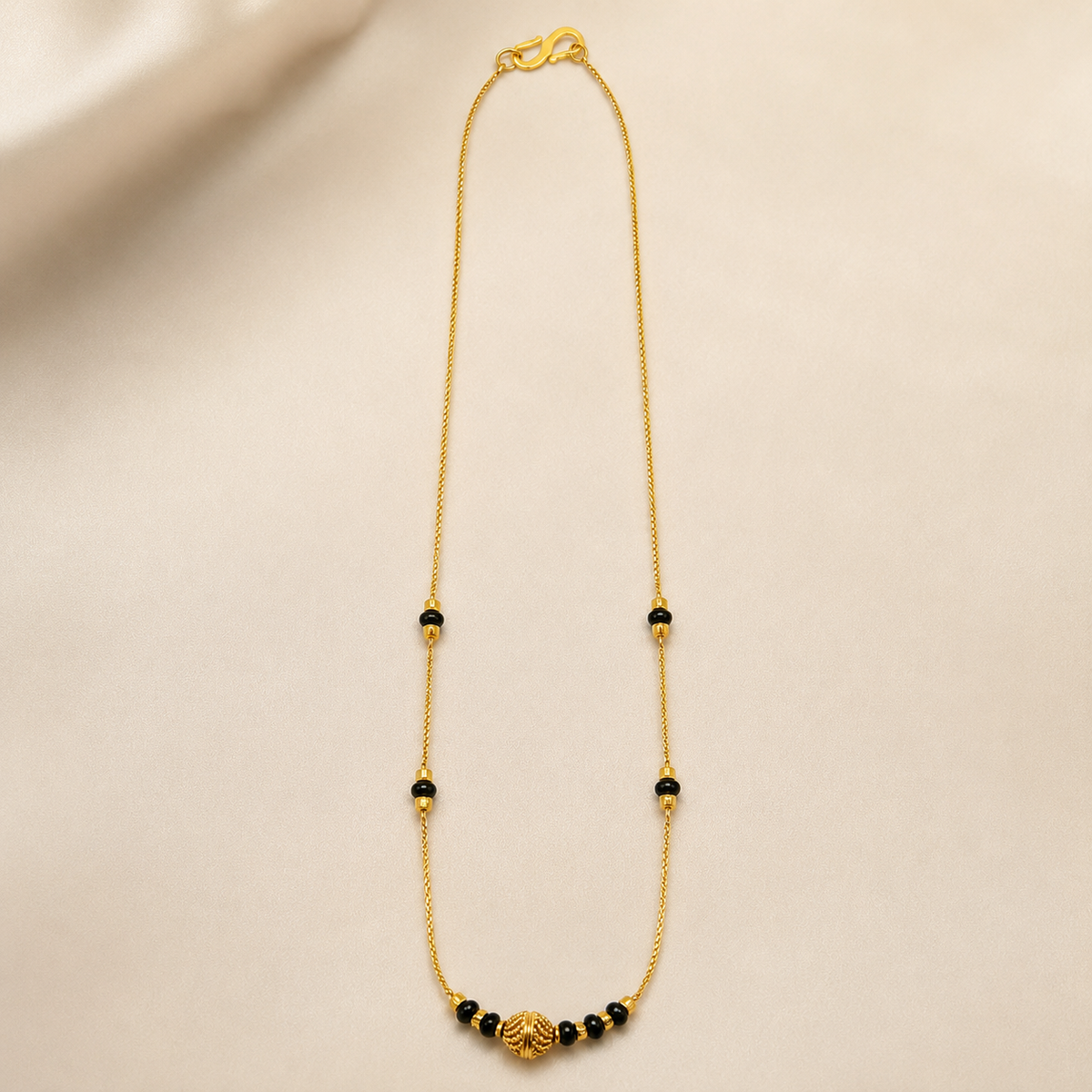 Textured-centre black bead mangalsutra arranged on cream fabric