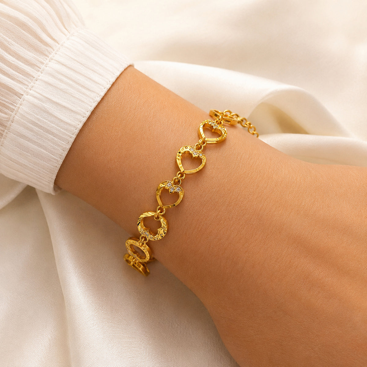 Open-heart link bracelet shown on a wrist beside a cream sleeve