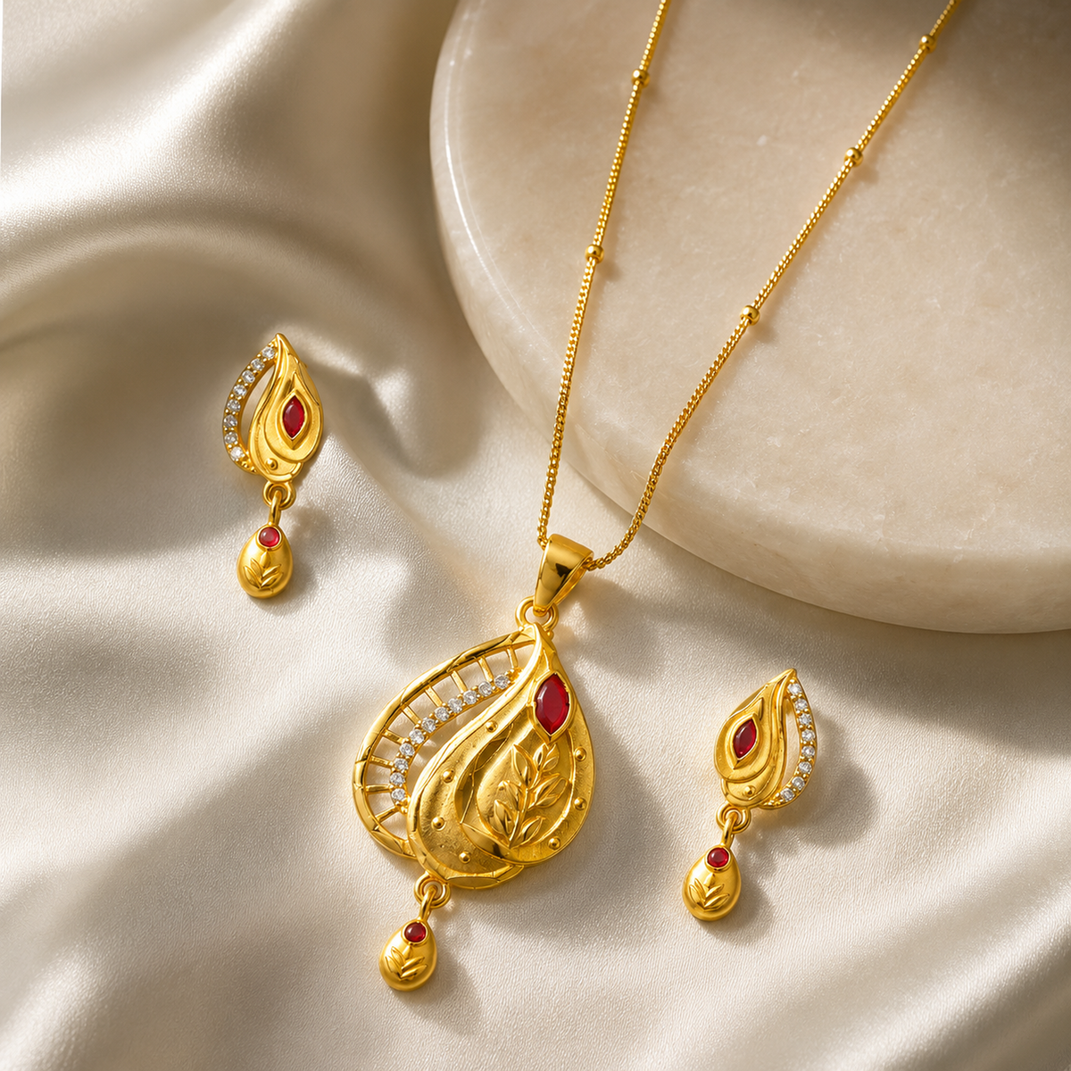 Leaf pendant and drop earrings arranged beside a cream display block